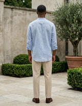 Man standing outdoors wearing a light blue shirt and beige pants.