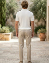 Man walking away in a white shirt and beige pants in a garden setting