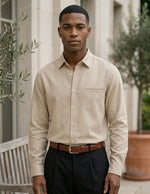 Man wearing a beige button-up shirt and dark pants standing outdoors.