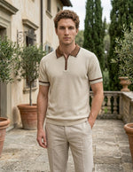 Man wearing a beige polo shirt and pants in an outdoor setting with greenery.