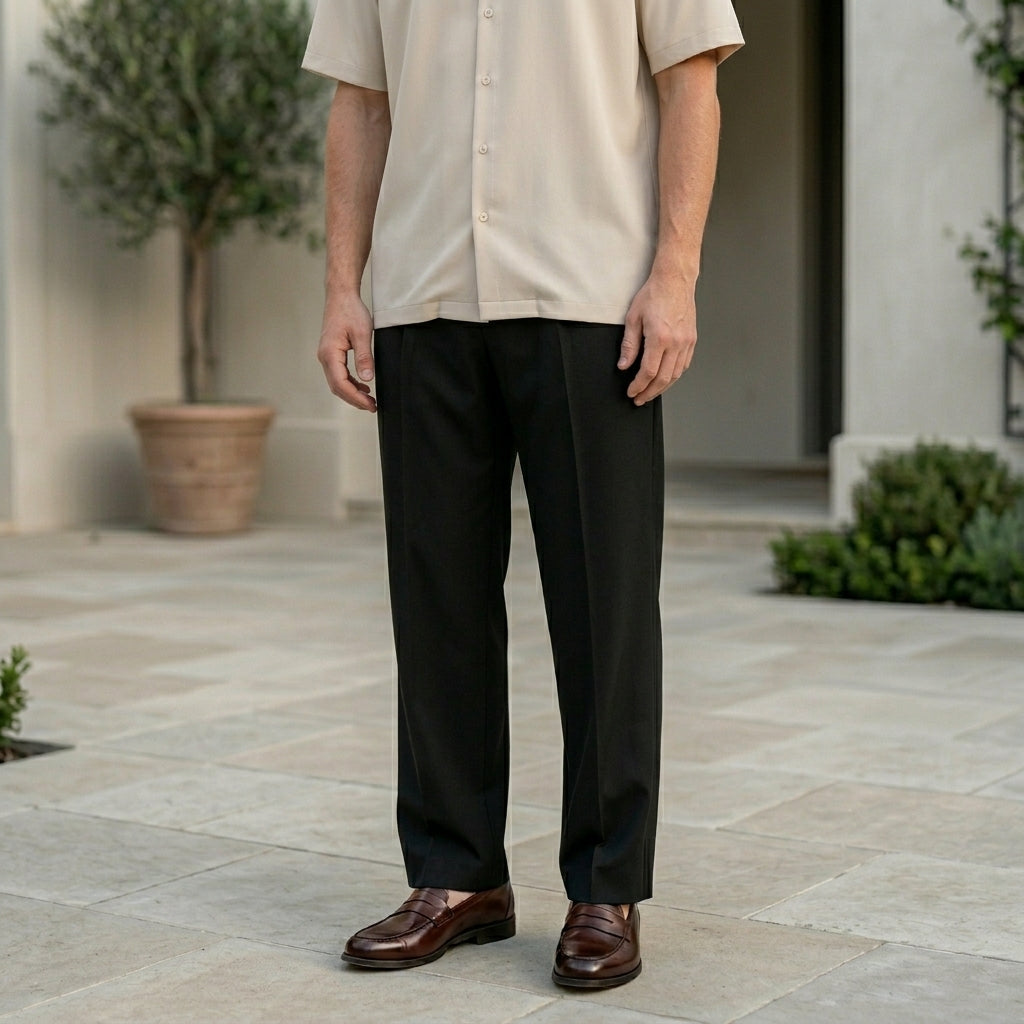 Man wearing a beige shirt and black pants standing on a stone patio.