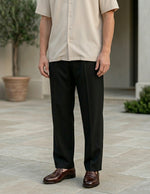 Man wearing a beige shirt and black pants standing on a stone patio.