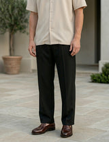Man wearing a beige shirt and black pants standing on a stone patio.