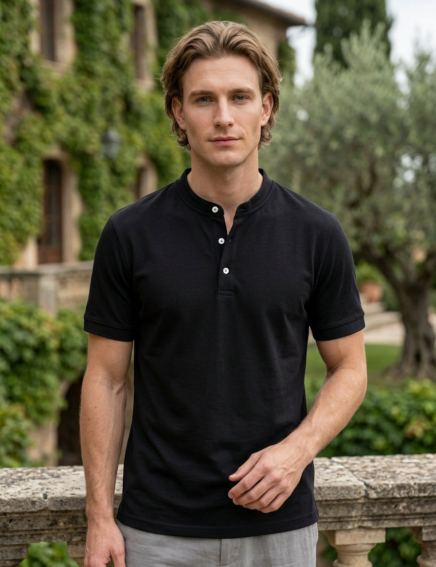 Man wearing a black polo shirt standing outdoors with greenery in the background