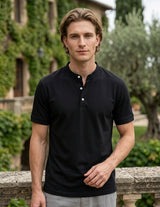 Man wearing a black polo shirt standing outdoors with greenery in the background