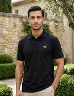 Man wearing a black polo shirt with a logo in an outdoor setting