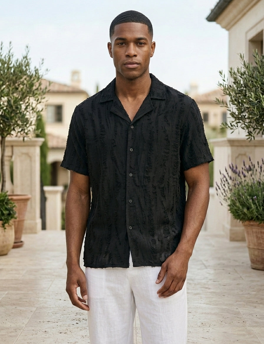Man wearing a black short-sleeve shirt and white pants standing outdoors.