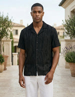 Man wearing a black short-sleeve shirt and white pants standing outdoors.