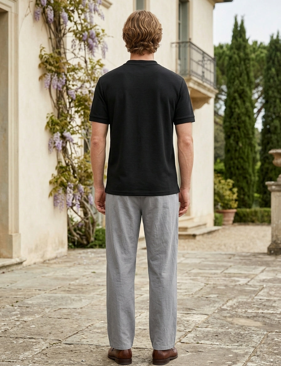 Man wearing a black t-shirt and gray pants standing in front of a classical building with decorative elements.