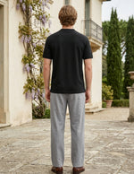 Man wearing a black t-shirt and gray pants standing in front of a classical building with decorative elements.