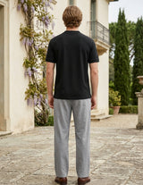 Man wearing a black t-shirt and gray pants standing in front of a classical building with decorative elements.