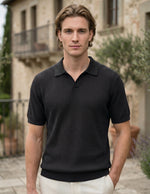 Man wearing a black textured polo shirt standing outdoors with a building and greenery in the background