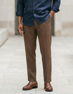 Man wearing a blue shirt, brown pants, and brown shoes on a light background