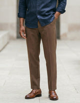 Man wearing a blue shirt, brown pants, and brown shoes on a light background