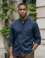 Man wearing a blue shirt standing outdoors with a building and greenery in the background