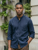 Man wearing a blue shirt standing outdoors with a building and greenery in the background