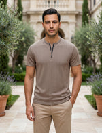 Man wearing a brown henley shirt and beige pants standing in a garden setting.