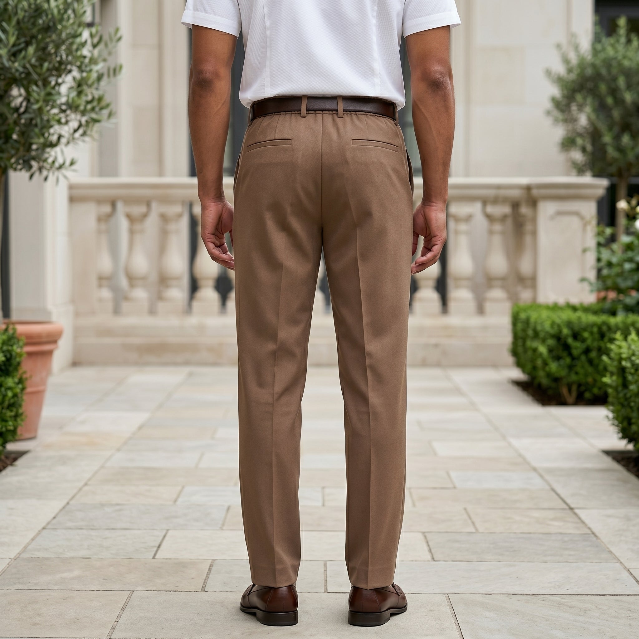 Man wearing a brown men’s pleated pocketed trousers with button waistband back view
