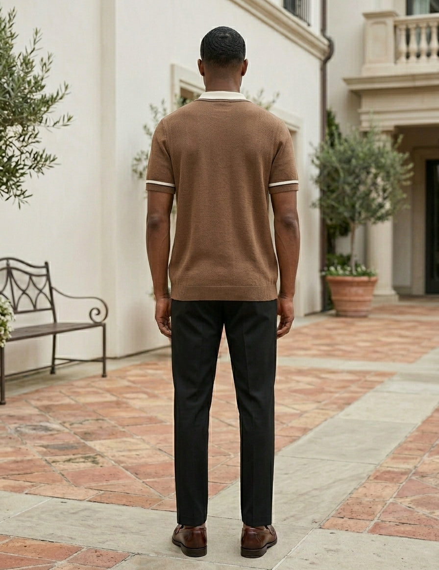 Man wearing a brown polo shirt and dark pants standing in an outdoor setting with a building and bench in the background.
