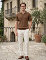 Man wearing a brown polo shirt and white pants standing in front of a stone building.