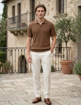 Man wearing a brown polo shirt and white pants standing in front of a stone building.