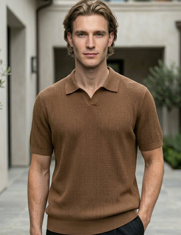 Man wearing a brown polo shirt standing in an outdoor setting with plants and a building.