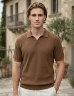Man wearing a brown polo shirt standing in front of a stone building.