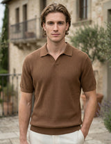 Man wearing a brown polo shirt standing in front of a stone building.