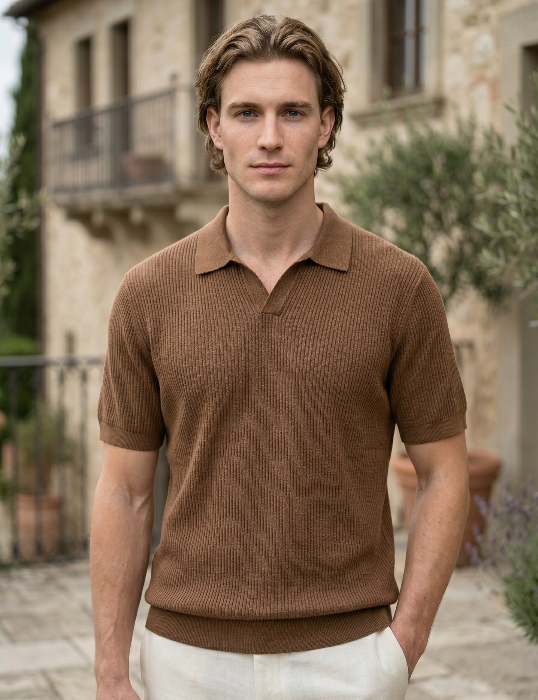 Man wearing a brown polo shirt standing in front of a stone building.