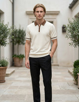 Man wearing a cream polo shirt with brown accents and black pants standing in an outdoor setting.