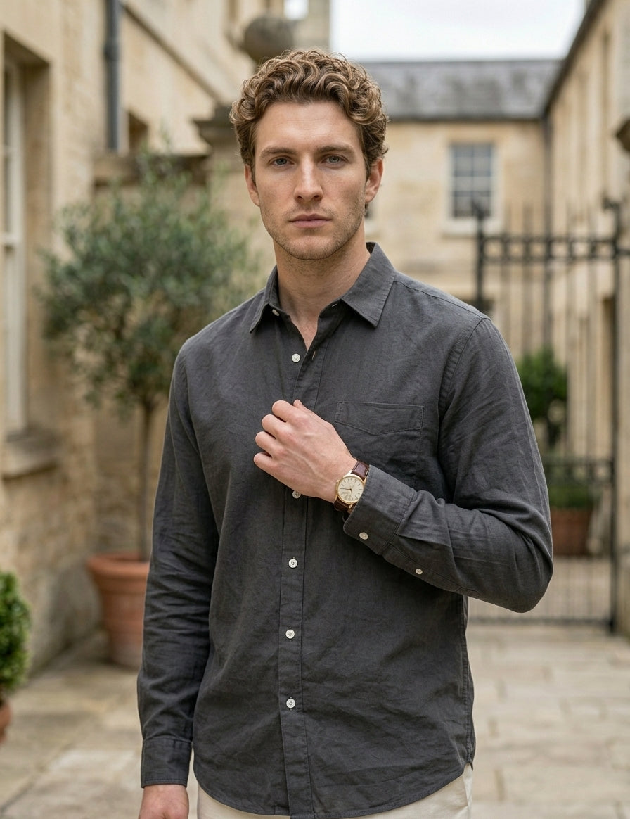 Man wearing a dark gray shirt outdoors with buildings and plants in the background