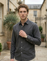 Man wearing a dark gray shirt outdoors with buildings and plants in the background