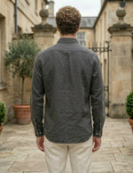 Man wearing a dark green shirt standing in an outdoor setting with stone buildings and potted plants.