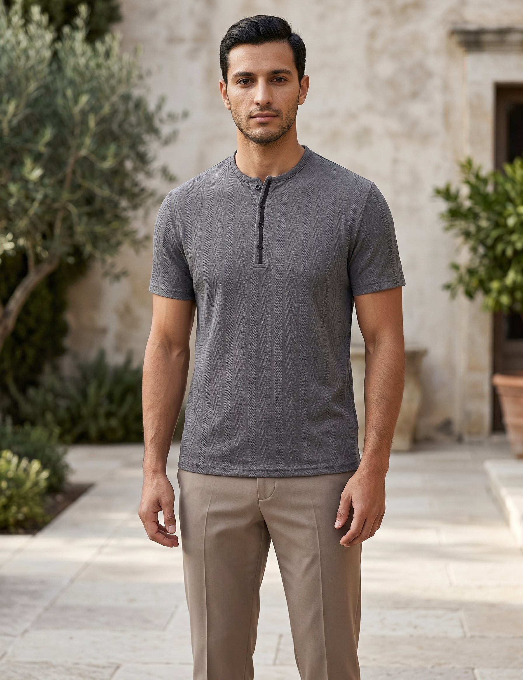 Man wearing a gray short-sleeve shirt and beige pants standing outdoors.