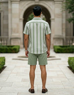 Man wearing a green and white striped shirt and shorts standing in front of a stone building.