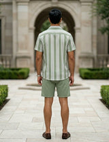 Man wearing a green and white striped shirt and shorts standing in front of a stone building.