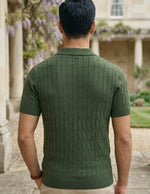 Man wearing a green knitted polo shirt standing in a garden with a building in the background