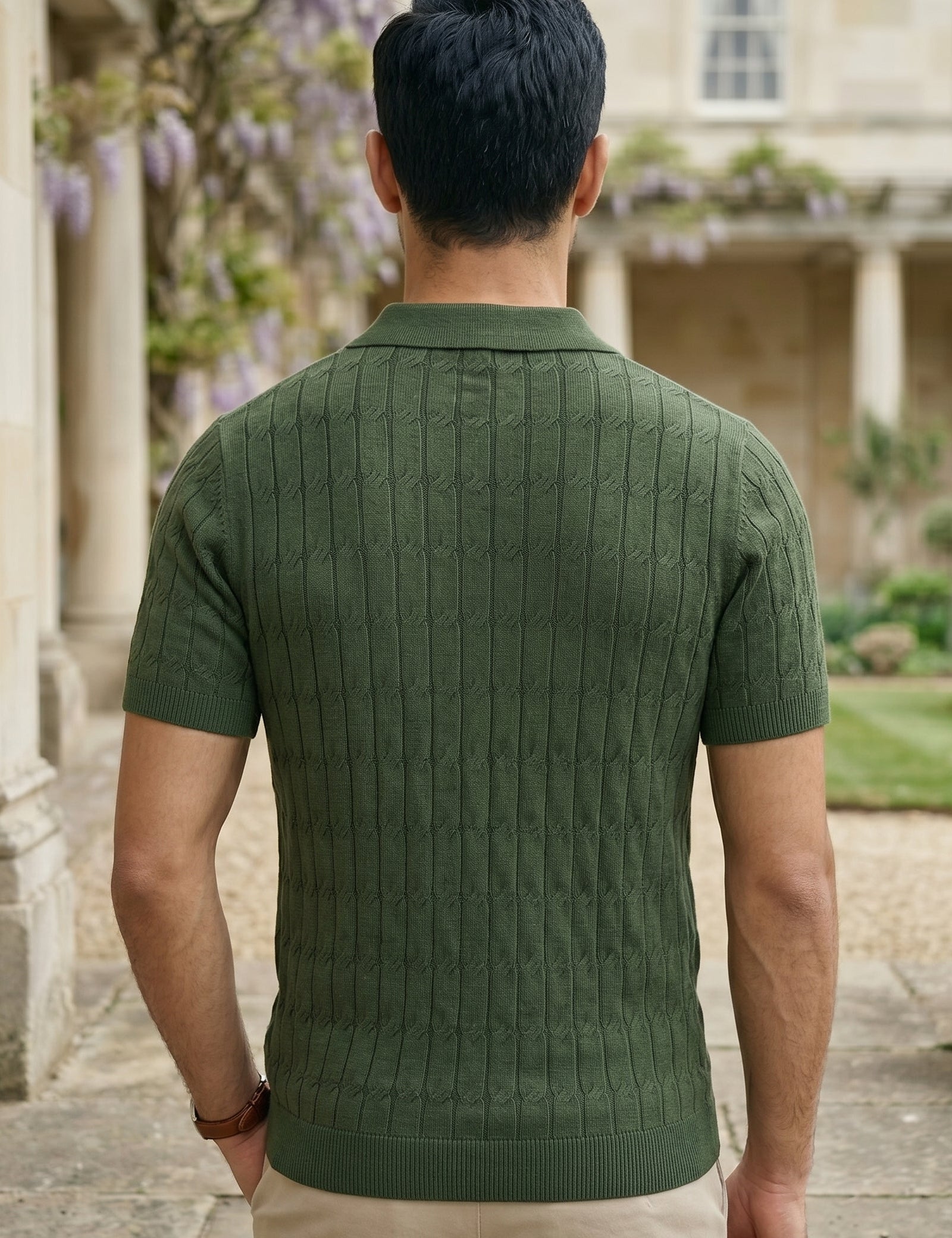 Man wearing a green knitted polo shirt standing in a garden with a building in the background