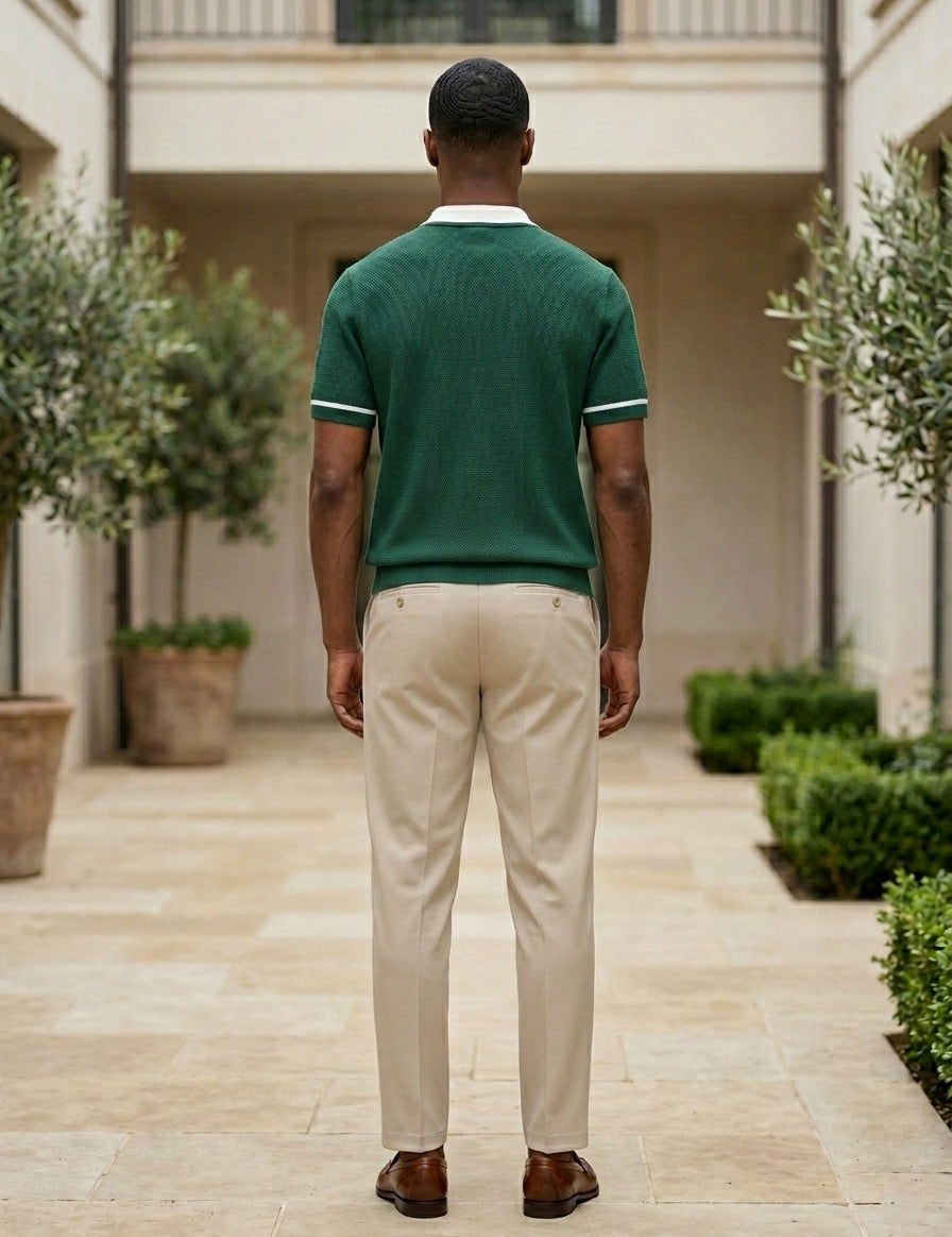 Man wearing a green polo shirt and beige pants standing in a courtyard with plants and a building.