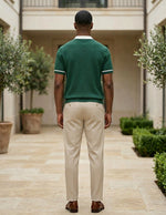 Man wearing a green polo shirt and beige pants standing in a courtyard with plants and a building.