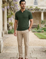 Man wearing a green polo shirt and beige pants standing in a garden setting.