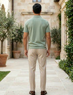 Man wearing a green polo shirt and beige pants walking away from the camera in an outdoor setting.