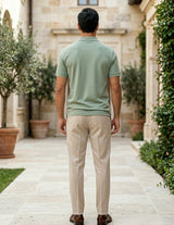 Man wearing a green polo shirt and beige pants walking away from the camera in an outdoor setting.