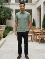 Man wearing a green polo shirt and black pants standing in an outdoor setting with tables and chairs.