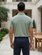 Man wearing a green polo shirt and dark pants standing in an outdoor setting.