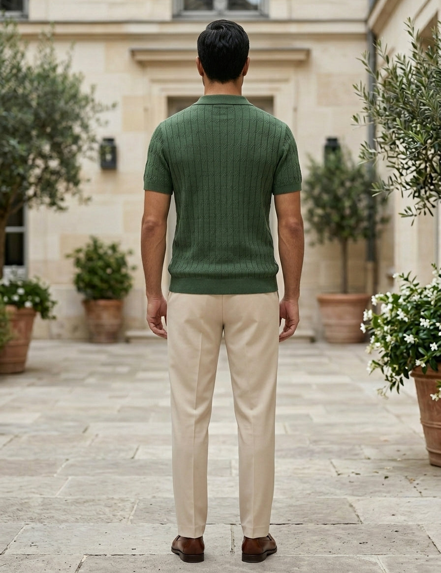 Man wearing a green sweater and beige pants standing in an outdoor setting with potted plants.