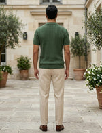 Man wearing a green sweater and beige pants standing in an outdoor setting with potted plants.