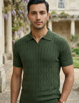Man wearing a green textured shirt standing outdoors with a building and garden in the background