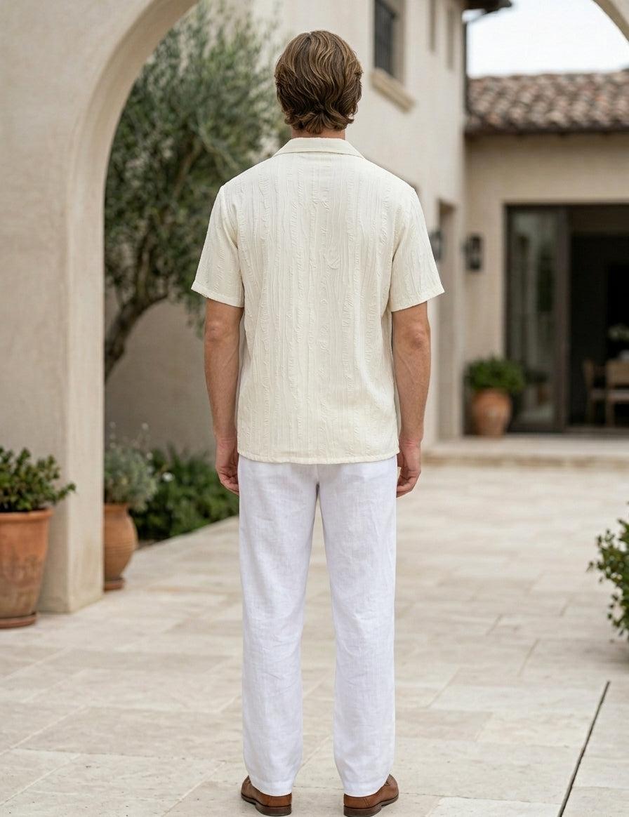 Man wearing a light-colored shirt and white pants standing in an outdoor setting.