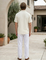 Man wearing a light-colored shirt and white pants standing in an outdoor setting.